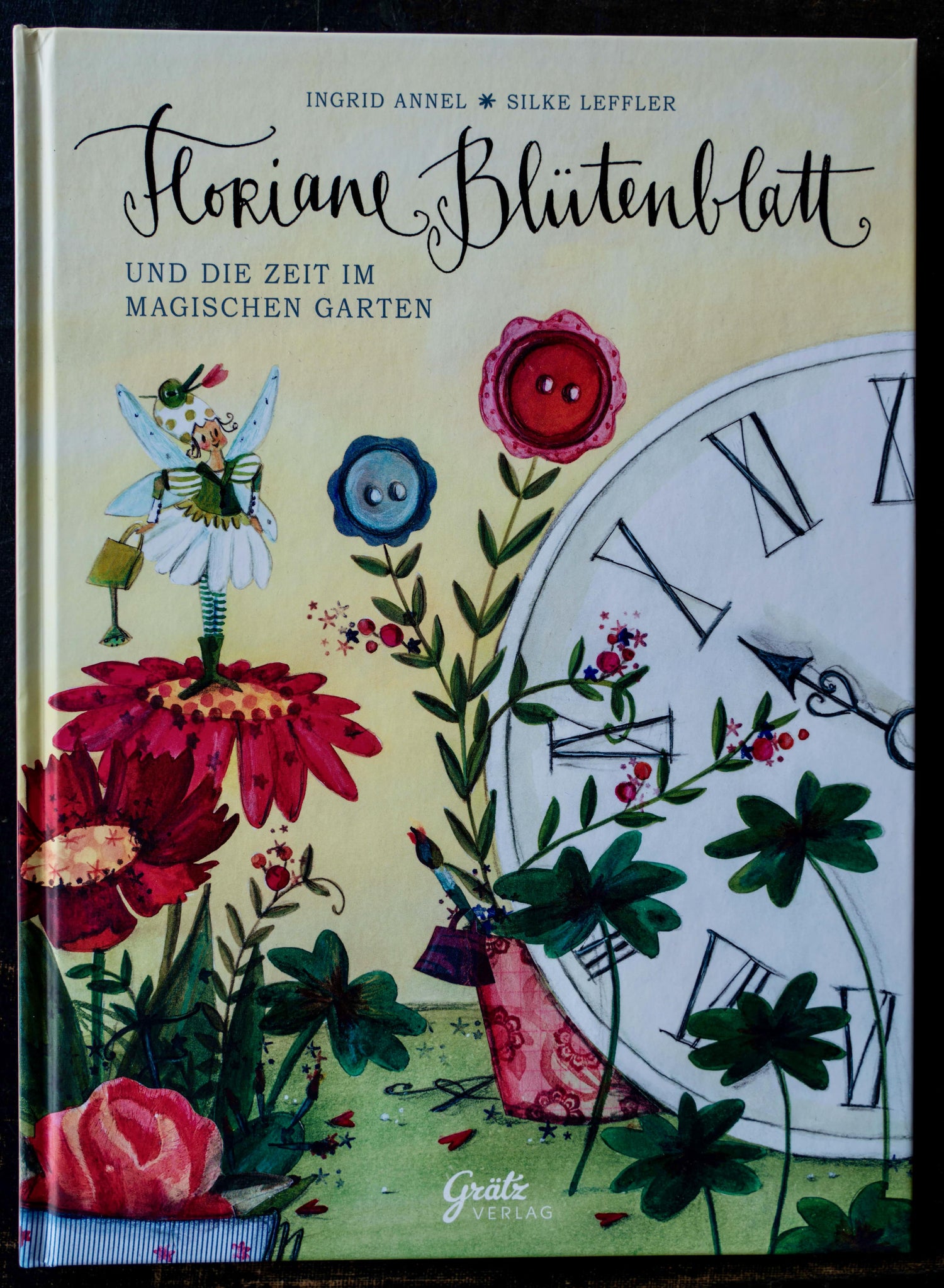 Buchcover „Floriane Blütenblatt und die Zeit im magischen Garten“ von Ingrid Annel und Silke Leffler mit verspielter Gartenillustration und einer Uhr, Grätz Verlag.